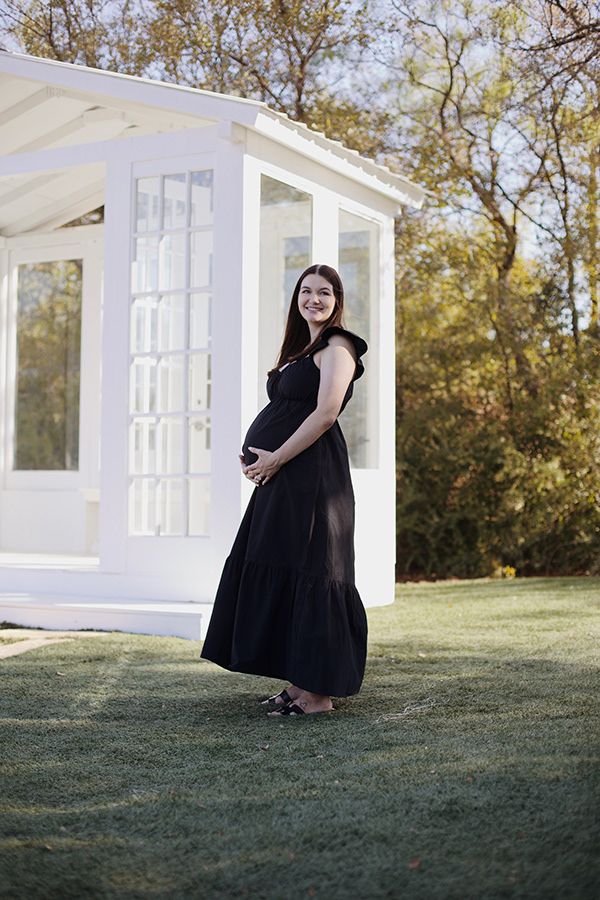Pregnant woman holding stomach near a glasshouse.