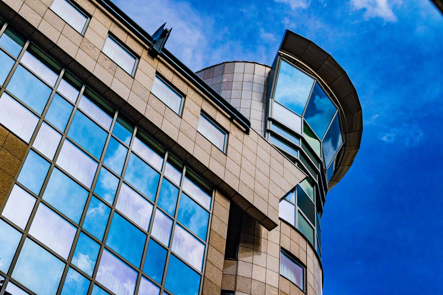 Modern office building with curved glass architecture against bright blue sky.