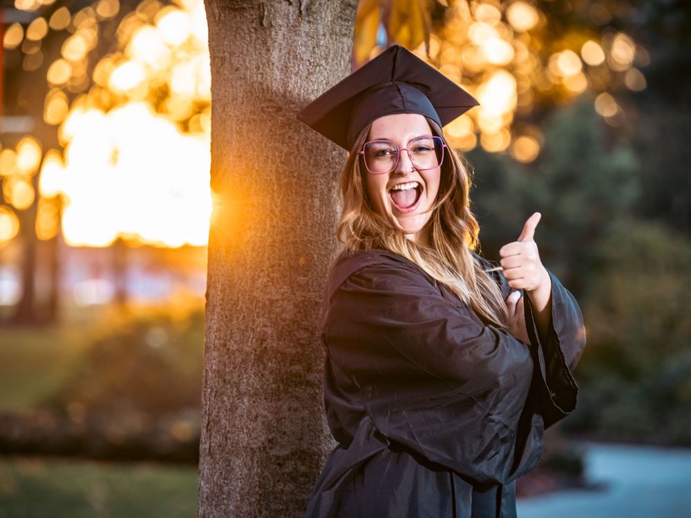 Enthusiastic graduate giving thumbs up during sunset graduation photoshoot.