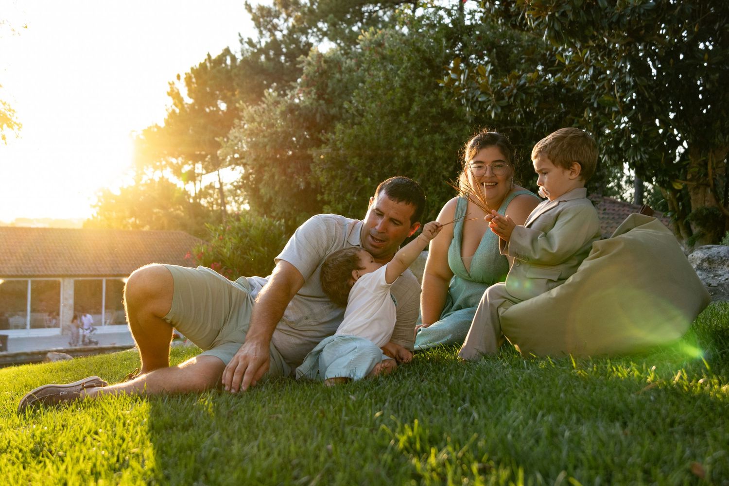 Family relaxing together on grass during golden hour sunset.