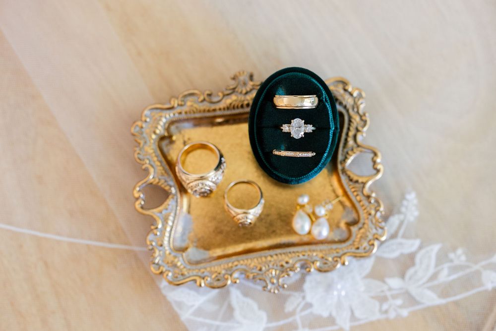 Wedding rings and jewelry box displayed on an ornate vintage gold tray against a light fabric background.