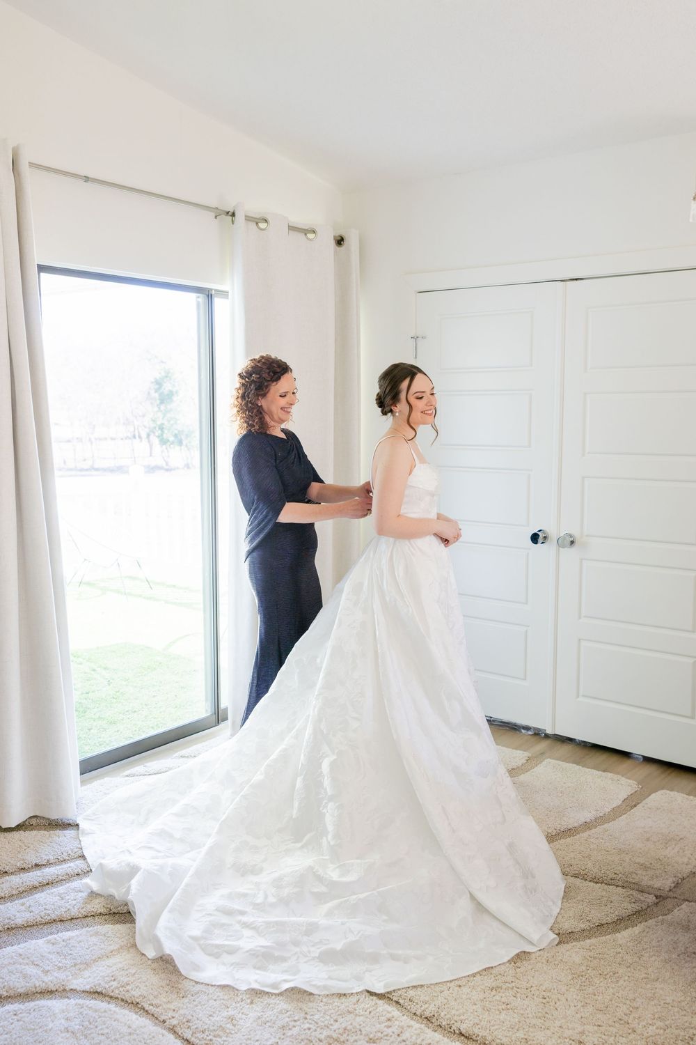 A wedding dress fitting shows the elegant long train of a white gown in a bright room.