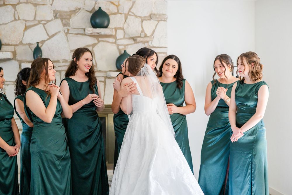 A bridal party wearing emerald green dresses shares a candid laughing moment with the bride in a white wedding gown.