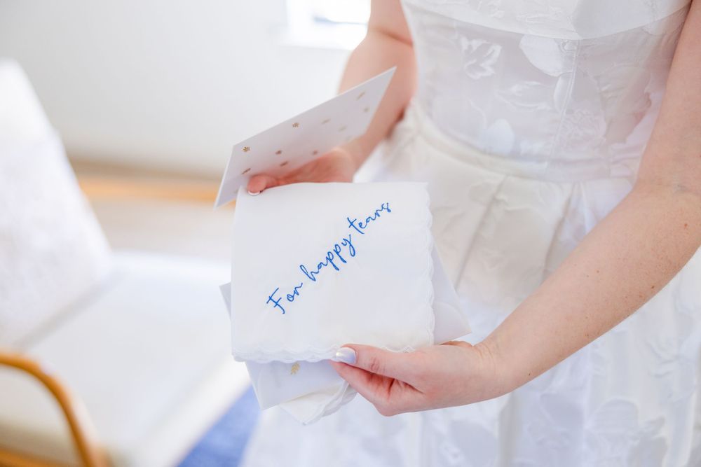 A white-clad figure holds a handwritten "For happy tears" note during what appears to be a wedding preparation moment.