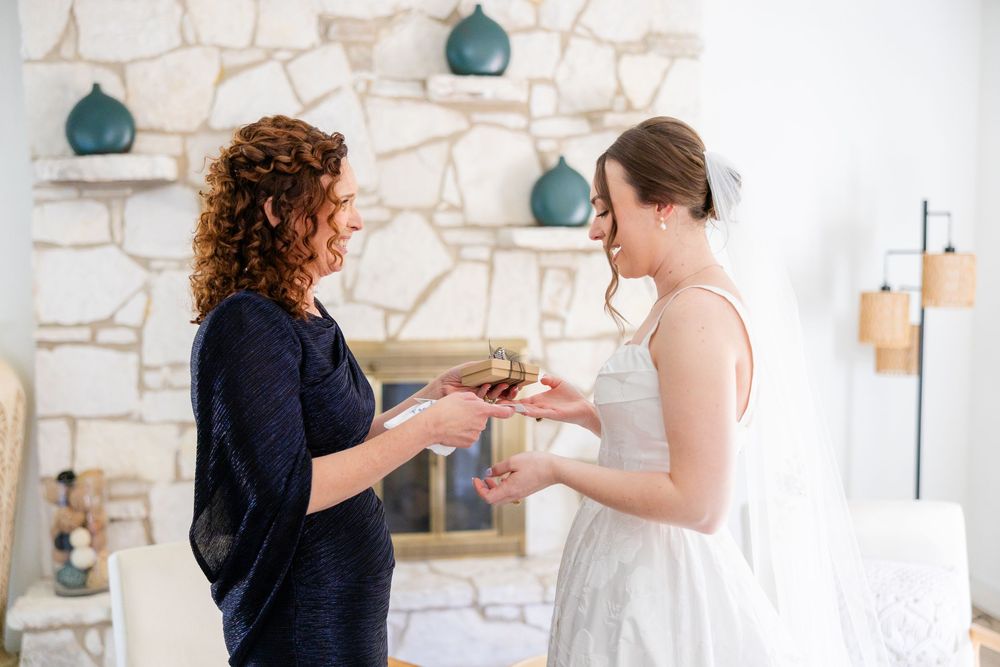 Two people in a white room with stone walls exchange a small item while standing near blue decorative vases on shelves.