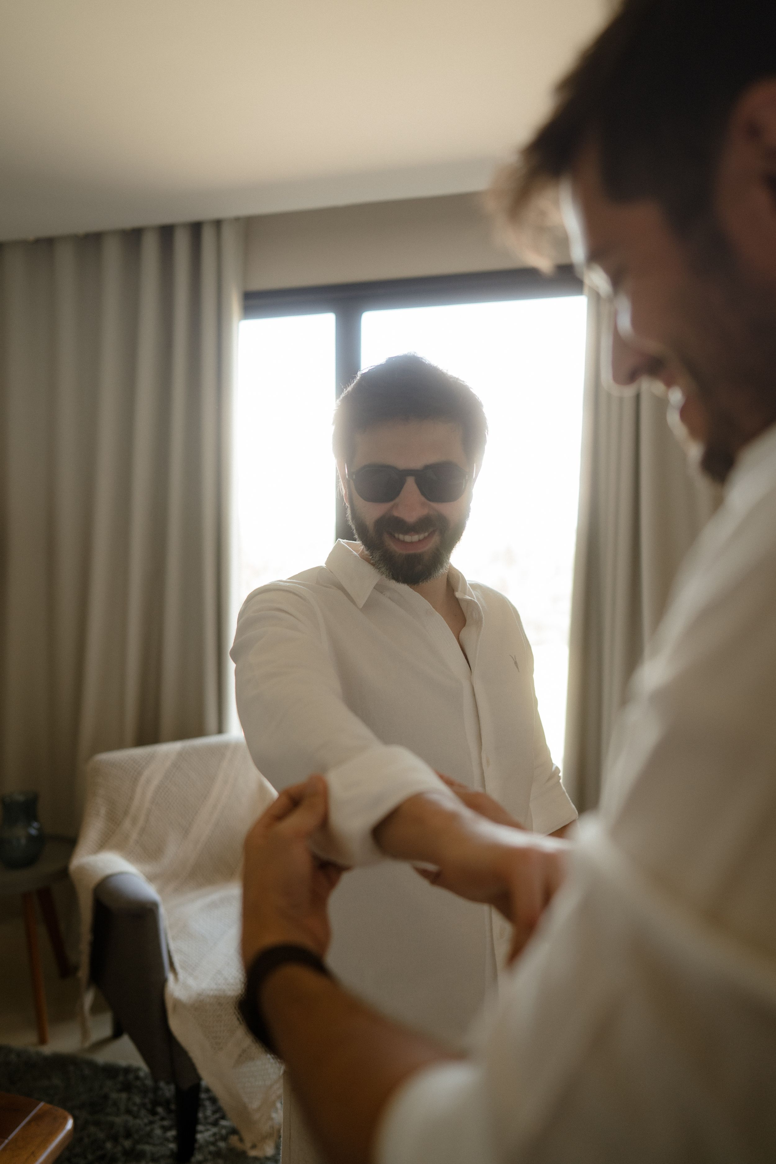 A sunlit room captures someone adjusting their white dress shirt sleeves.