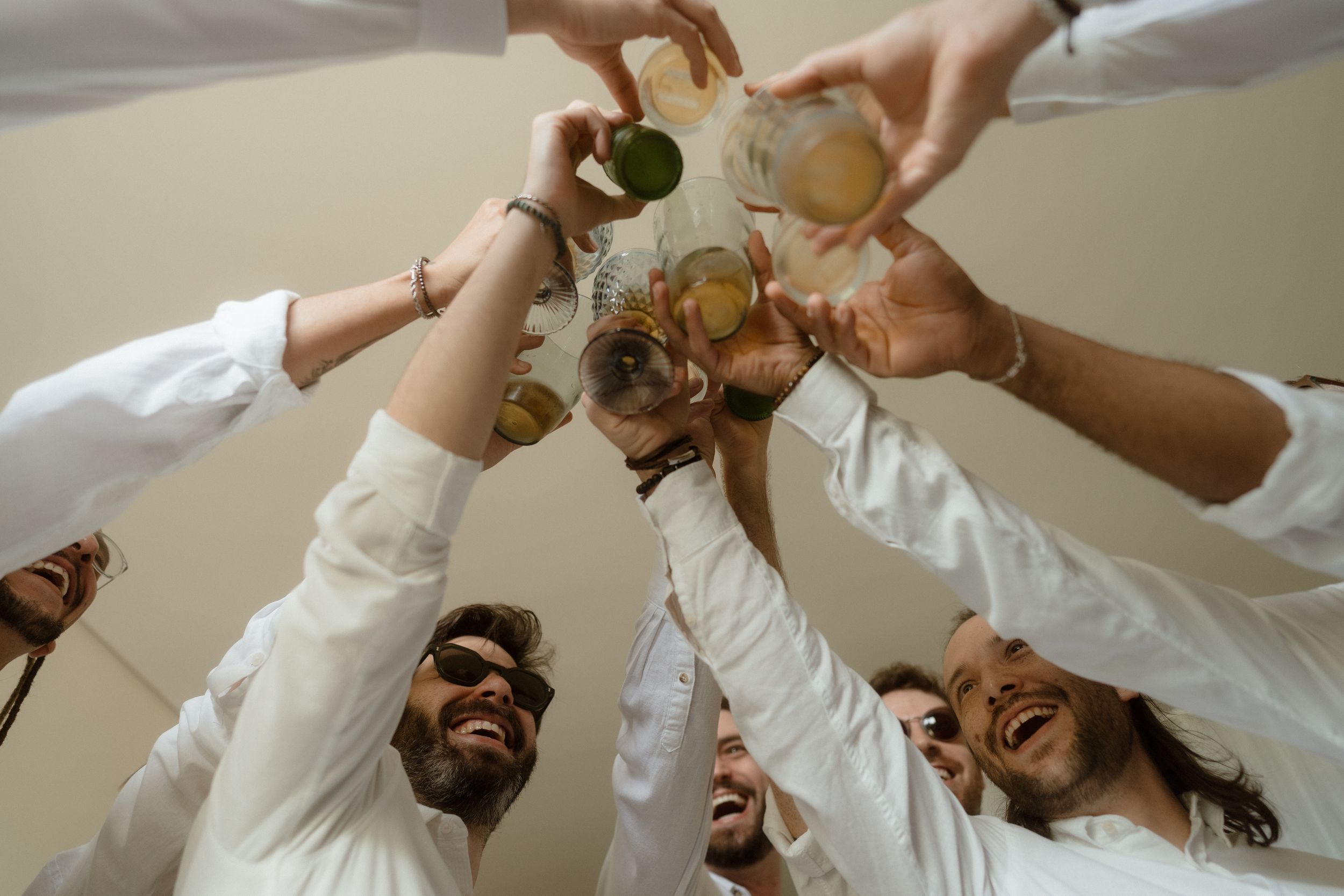 Wedding party in white shirts toasting with champagne glasses from below angle.