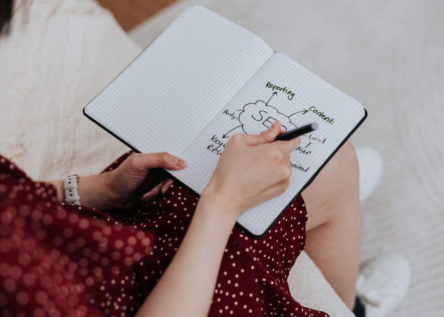 A person in a polka dot dress writes in a notebook while sitting down.