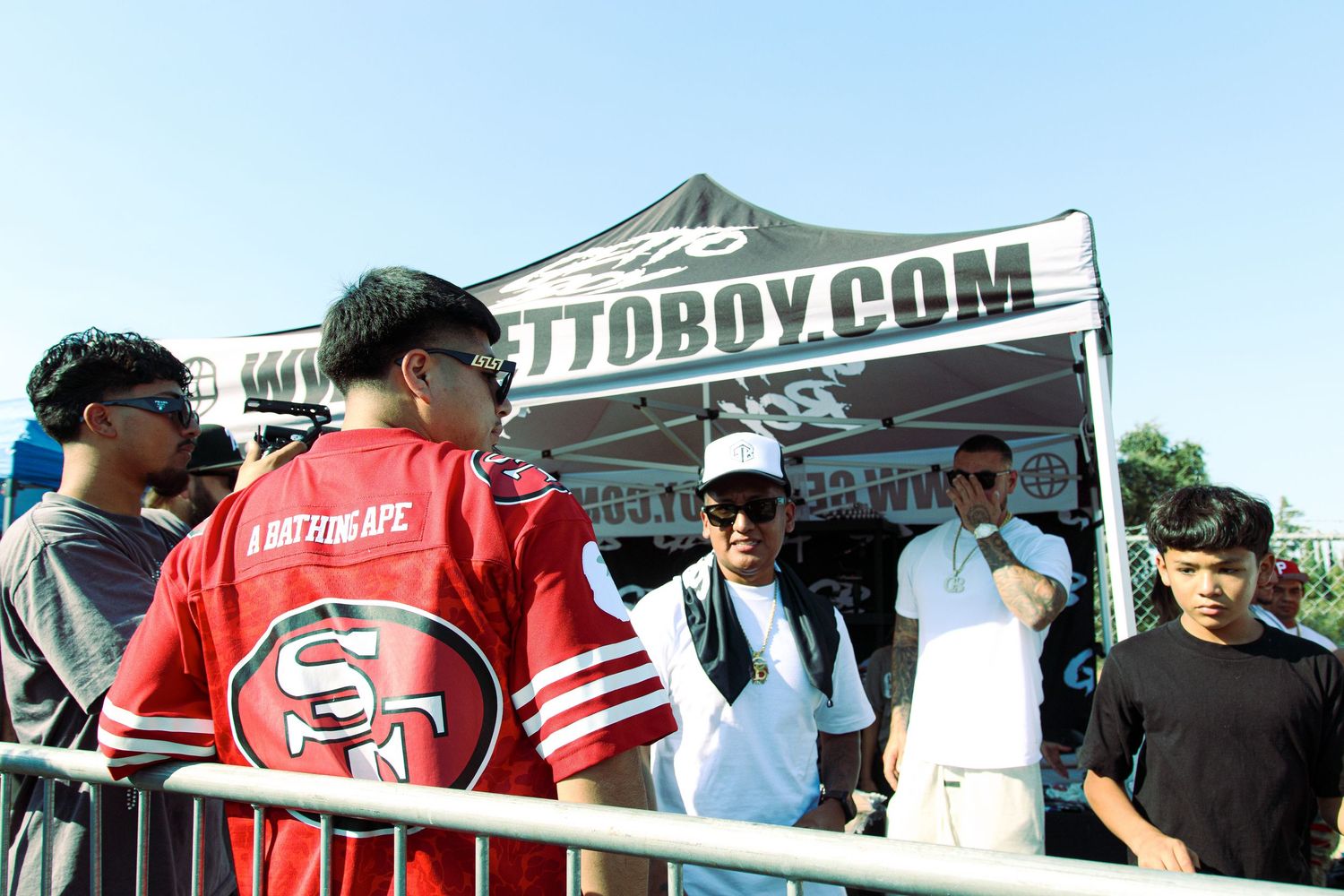 Young people gathering at Ghettoboy.com branded tent at an outdoor hip-hop event.