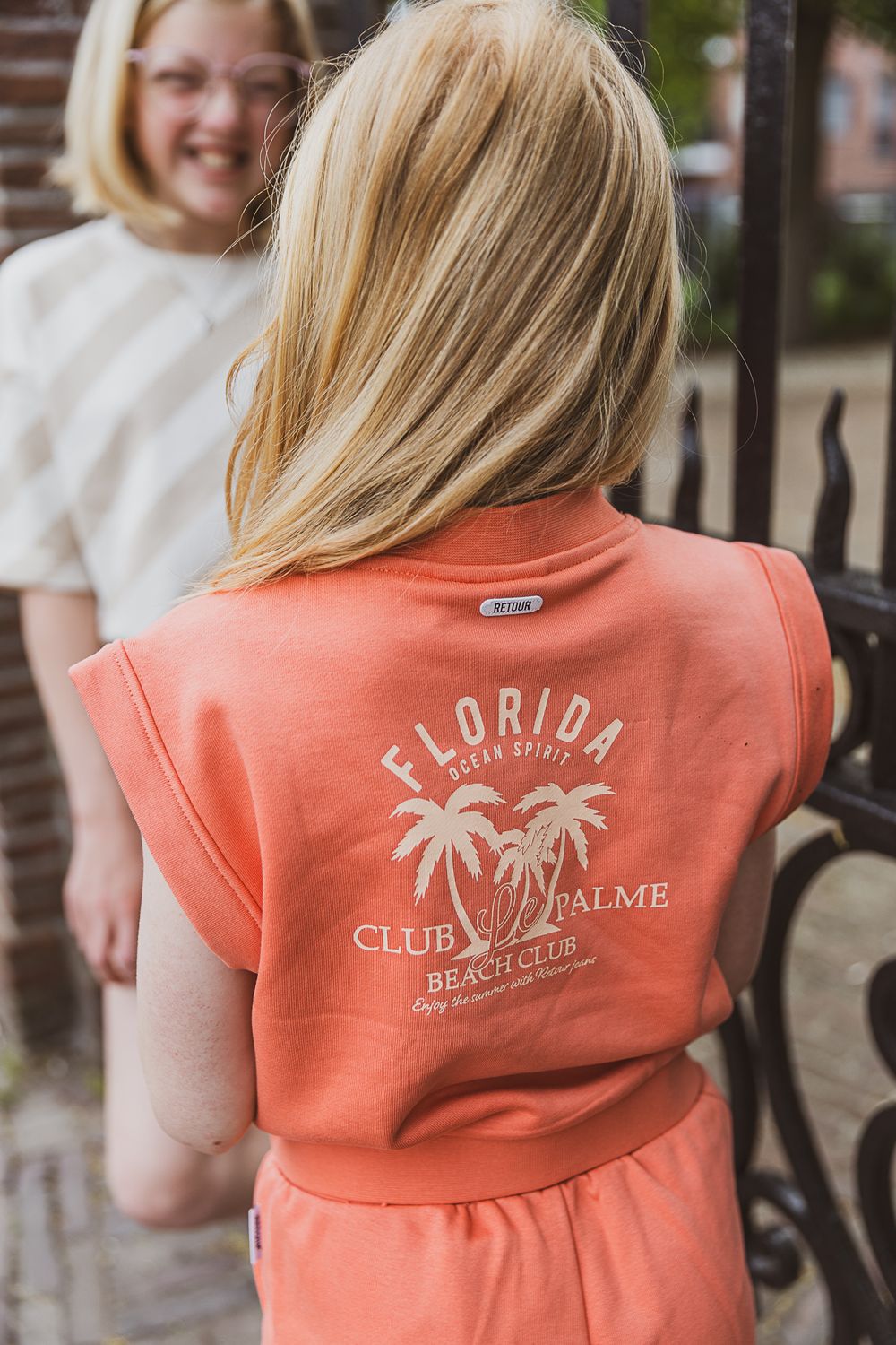 Back view of a coral colored t-shirt with a Florida Club palm tree beach design printed on it.
