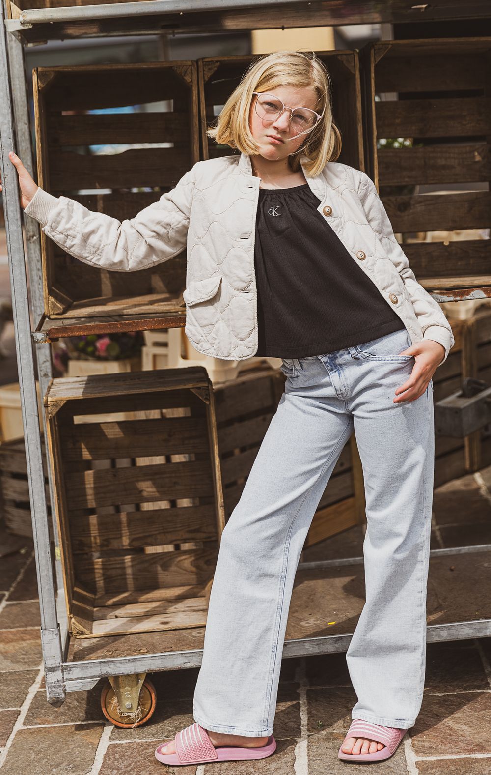 Casual outfit featuring light wash wide-leg jeans, white jacket, black top and pink sandals with rustic backdrop.