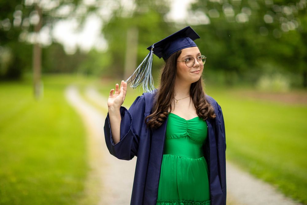 Graduate in navy cap and gown plays with tassel while standing outdoors.