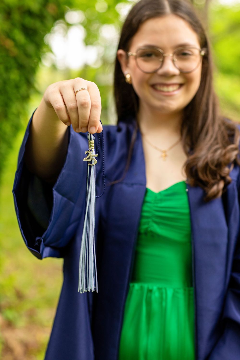 Graduate holding tassel while wearing navy graduation gown and emerald dress.