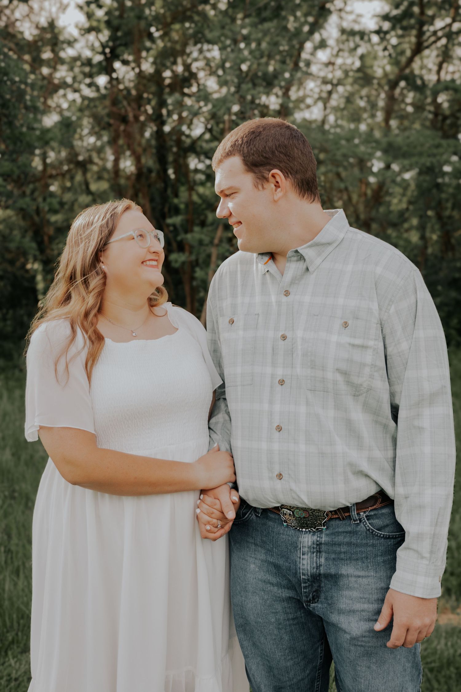 A couple shares a tender moment while holding hands outdoors in a natural wooded setting.