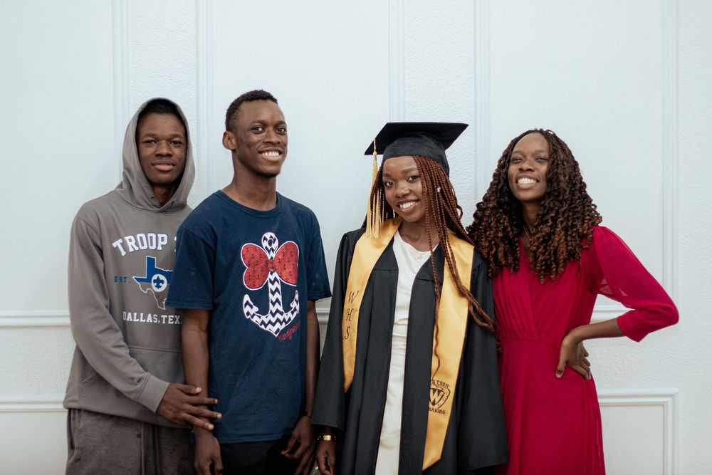 A group of four people standing together and smiling, with one wearing graduation regalia with gold stole.