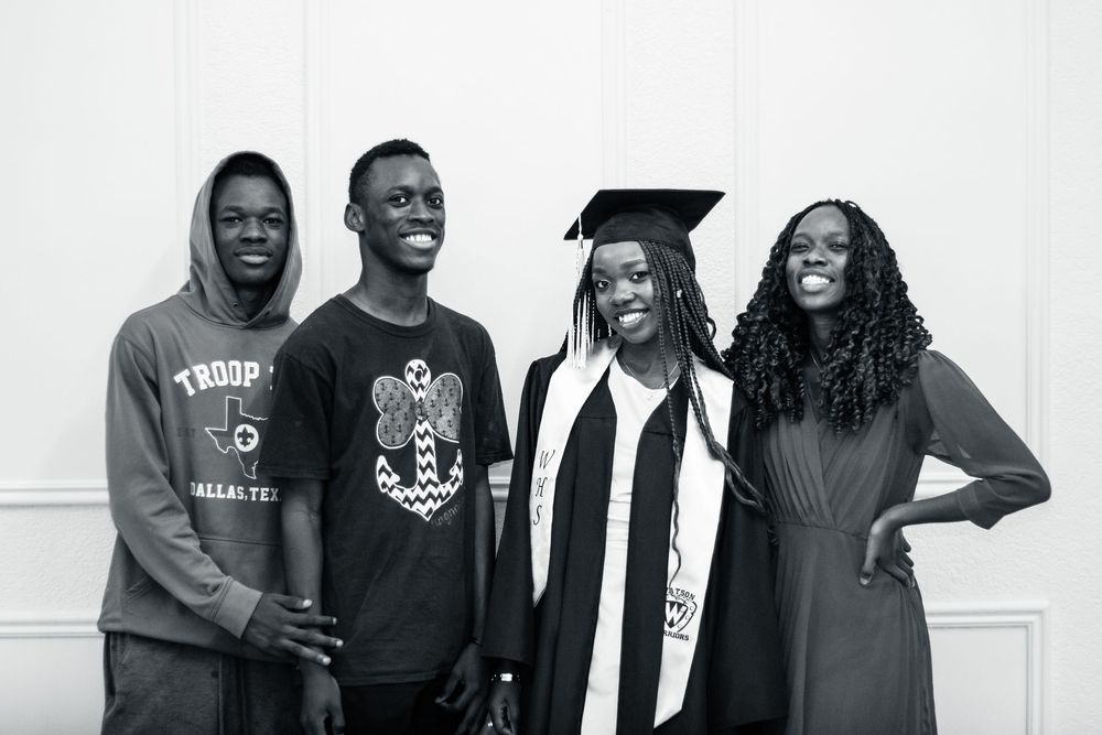 Black and white graduation portrait showing four people standing together smiling in casual and formal attire.
