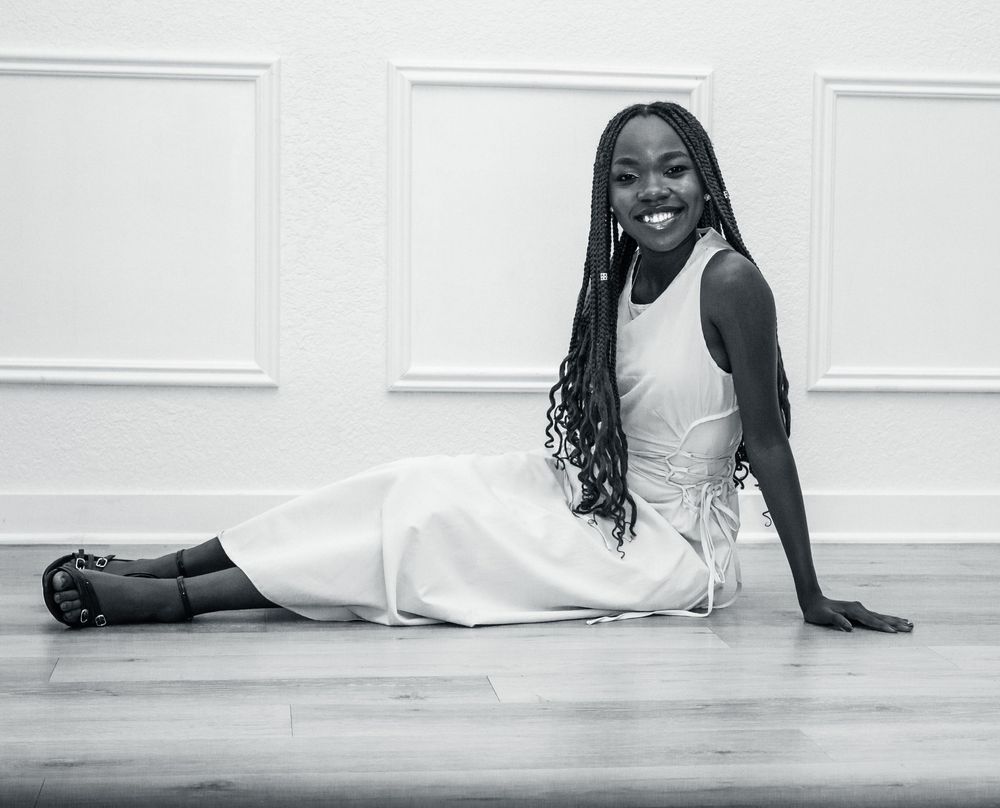 Black and white portrait of a graduate in an elegant white dress laying gracefully on a hardwood floor.