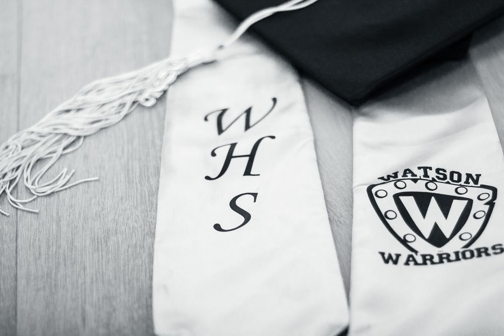 Black and white closeup of graduation cap and gown showing WHS embroidery and Warriors patch.