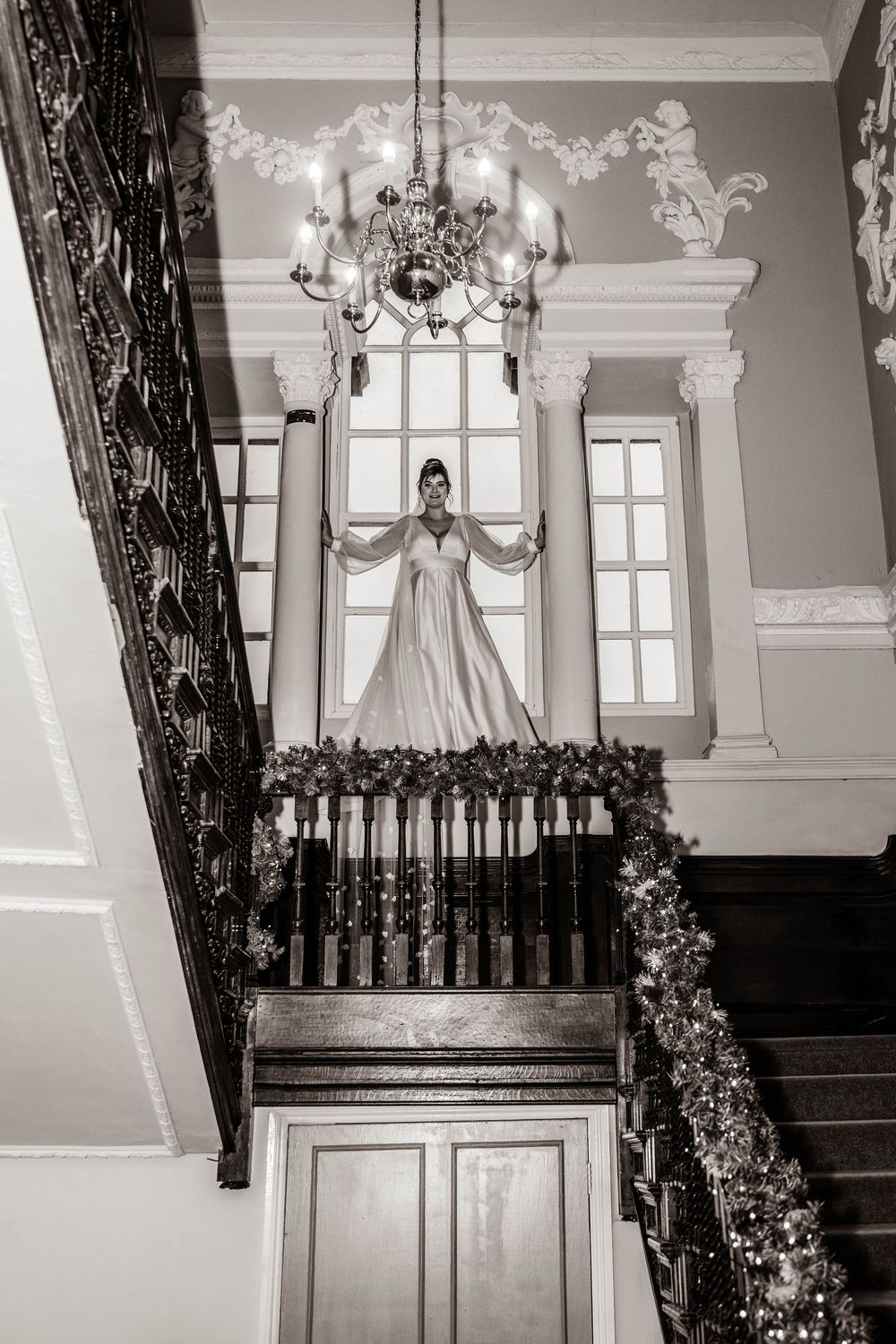 Black and white photo of bride posing on grand staircase with ornate architectural details.