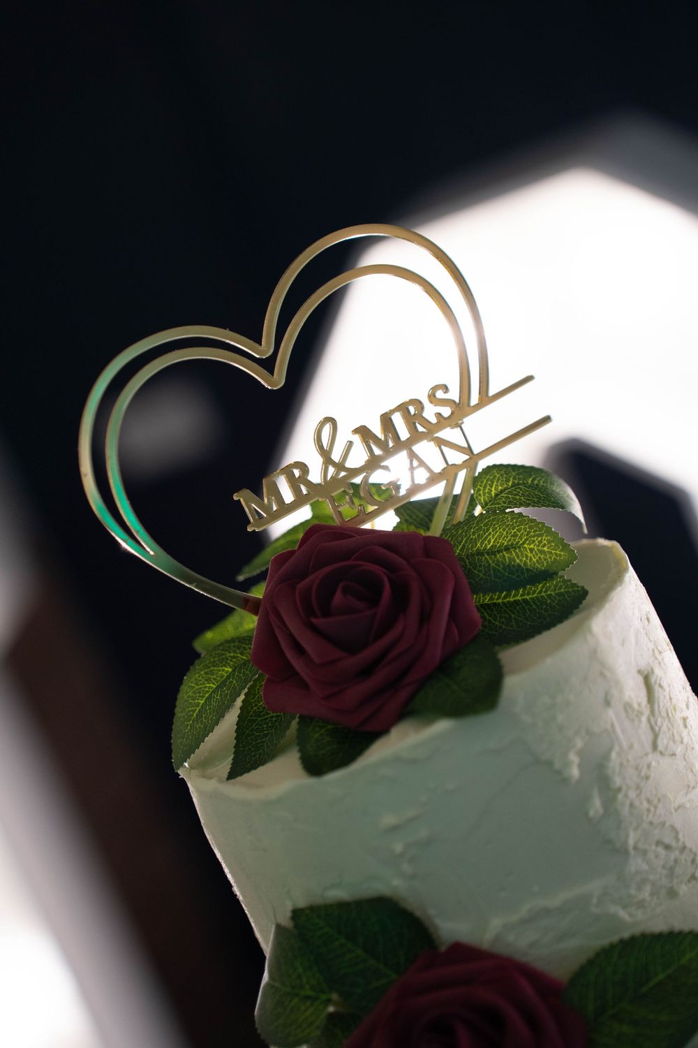 Wedding cake topper featuring Mr & Mrs text with burgundy roses and greenery.