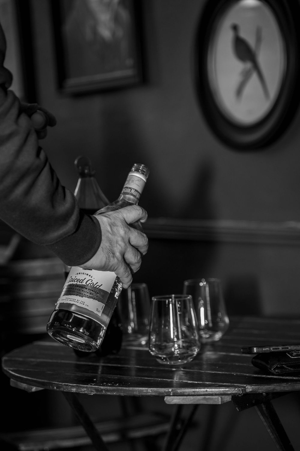 Hands pouring a bottle of spirits into glasses on a dark wooden table.