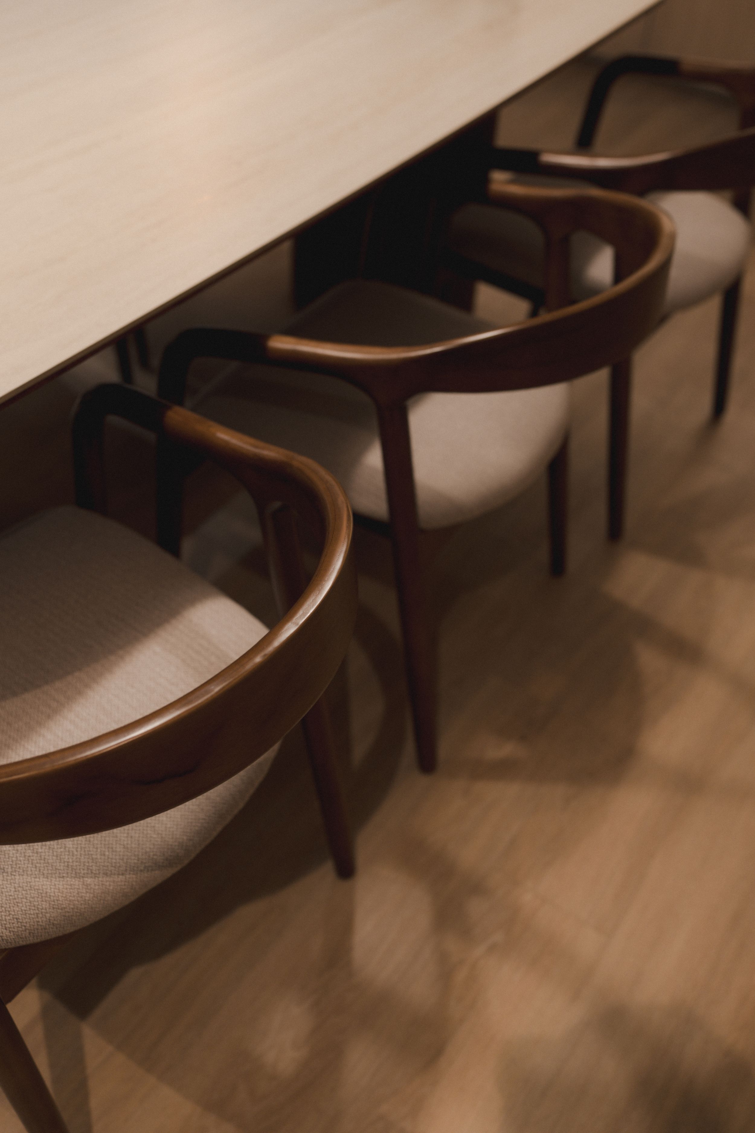A row of elegant curved wooden chairs with cream-colored upholstery sits against a wall in dim lighting.