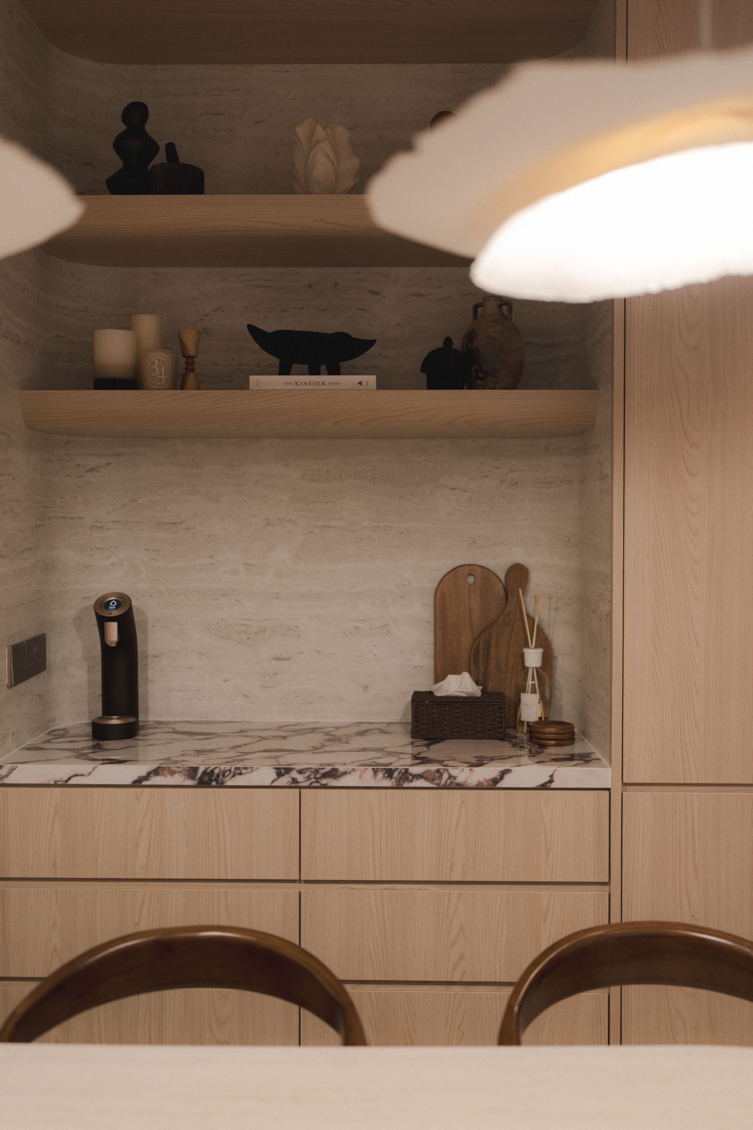 Modern kitchen shelving with decorative objects and a marble countertop against light wood cabinetry in warm ambient lighting.