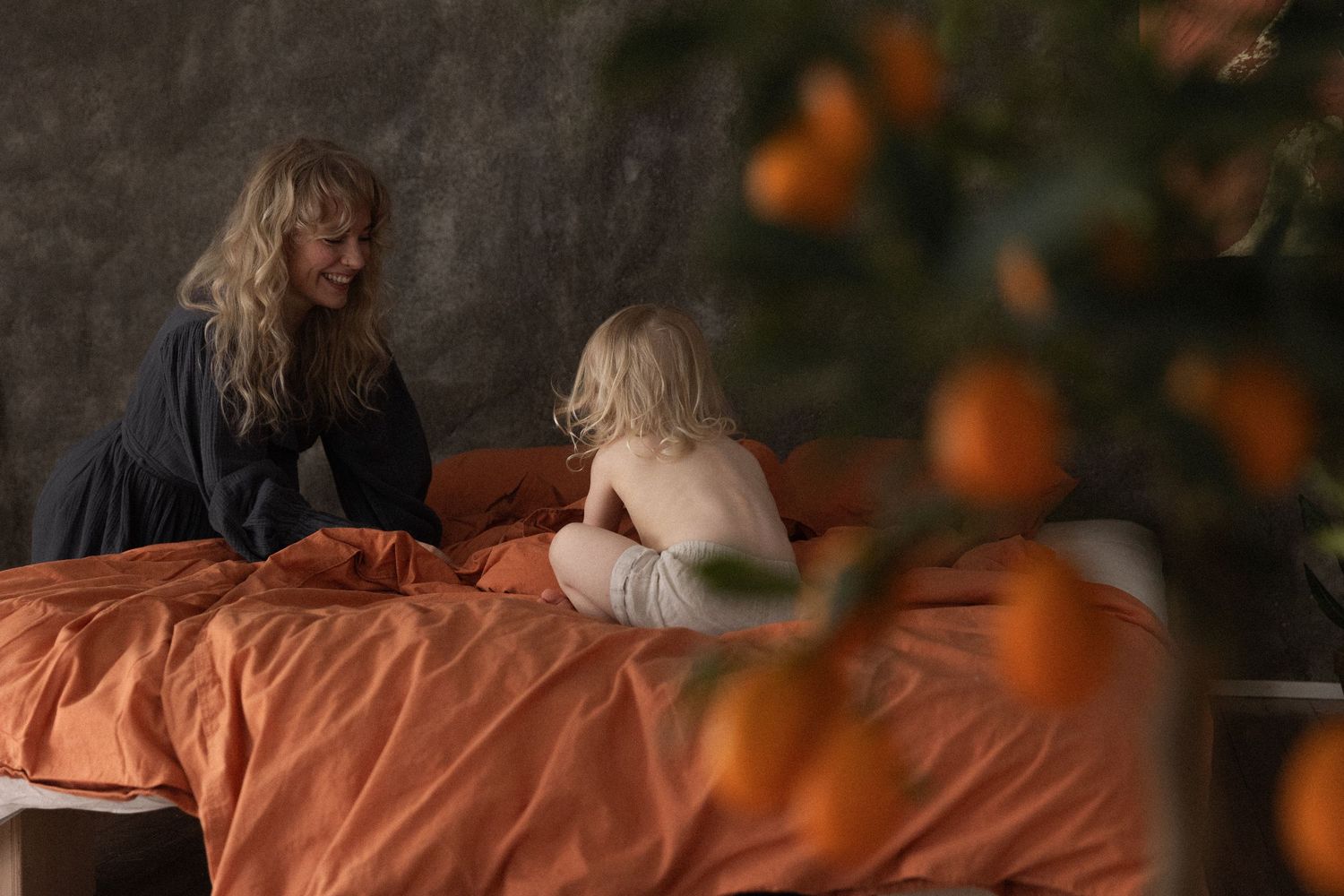 Two people sitting on an orange bedspread surrounded by blurred orange autumn decorations in a cozy indoor setting.