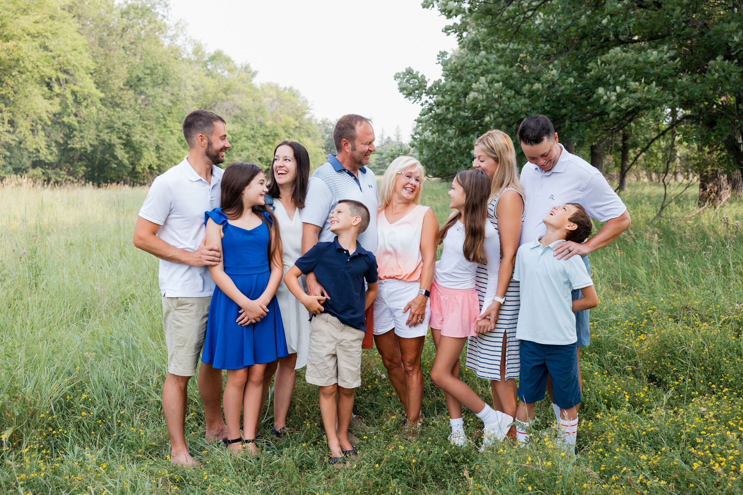 A group of eight people in coordinating blue, white and pink outfits stand together in a sunny meadow.