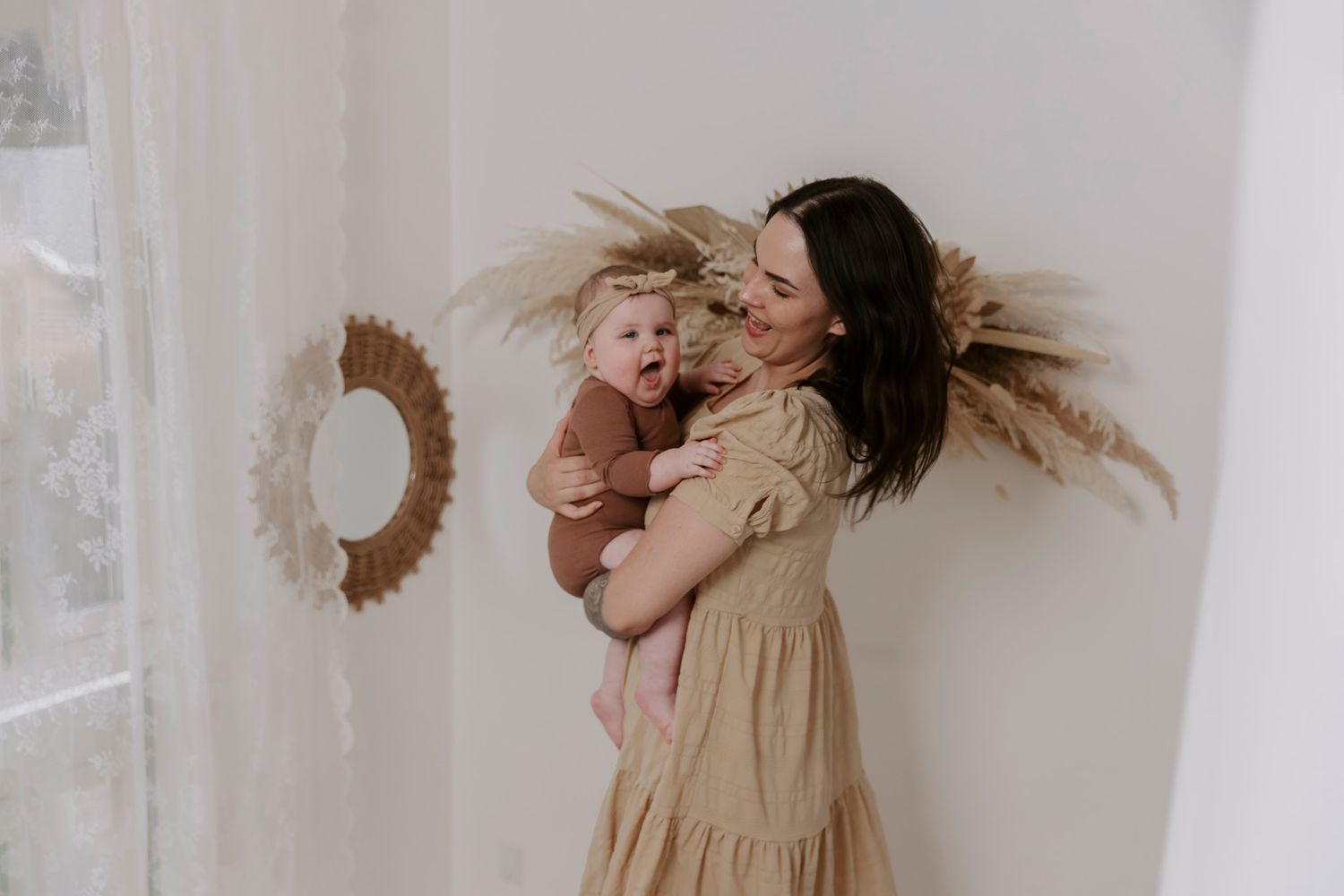 En baby i beige kjole liggende på hvid baggrund med pampasgræs som dekoration. Børnefotograf Fyn