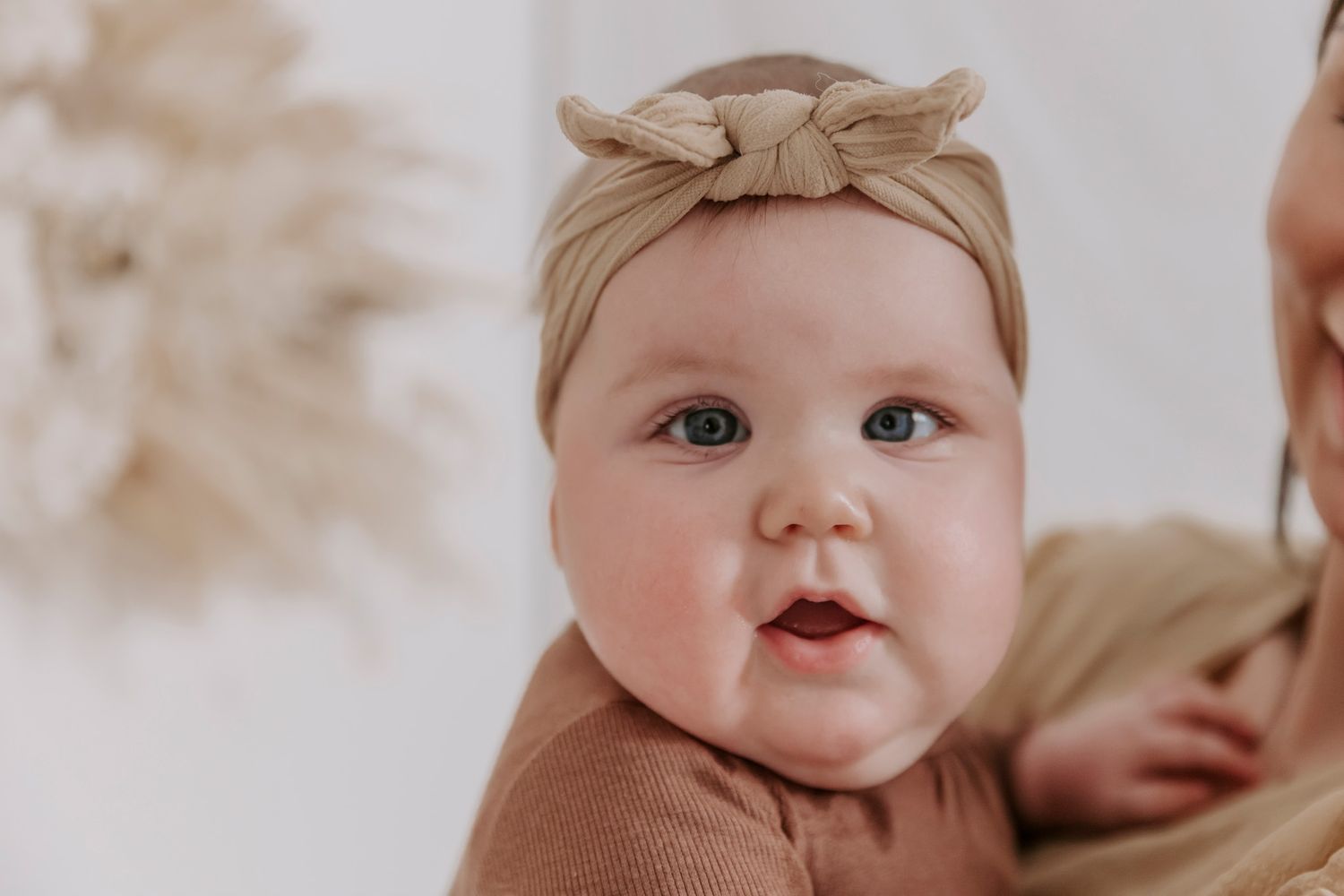 Close-up af en baby iført beige sløjfe-hårbånd foran en neutral baggrund. Børnefotograf Fyn