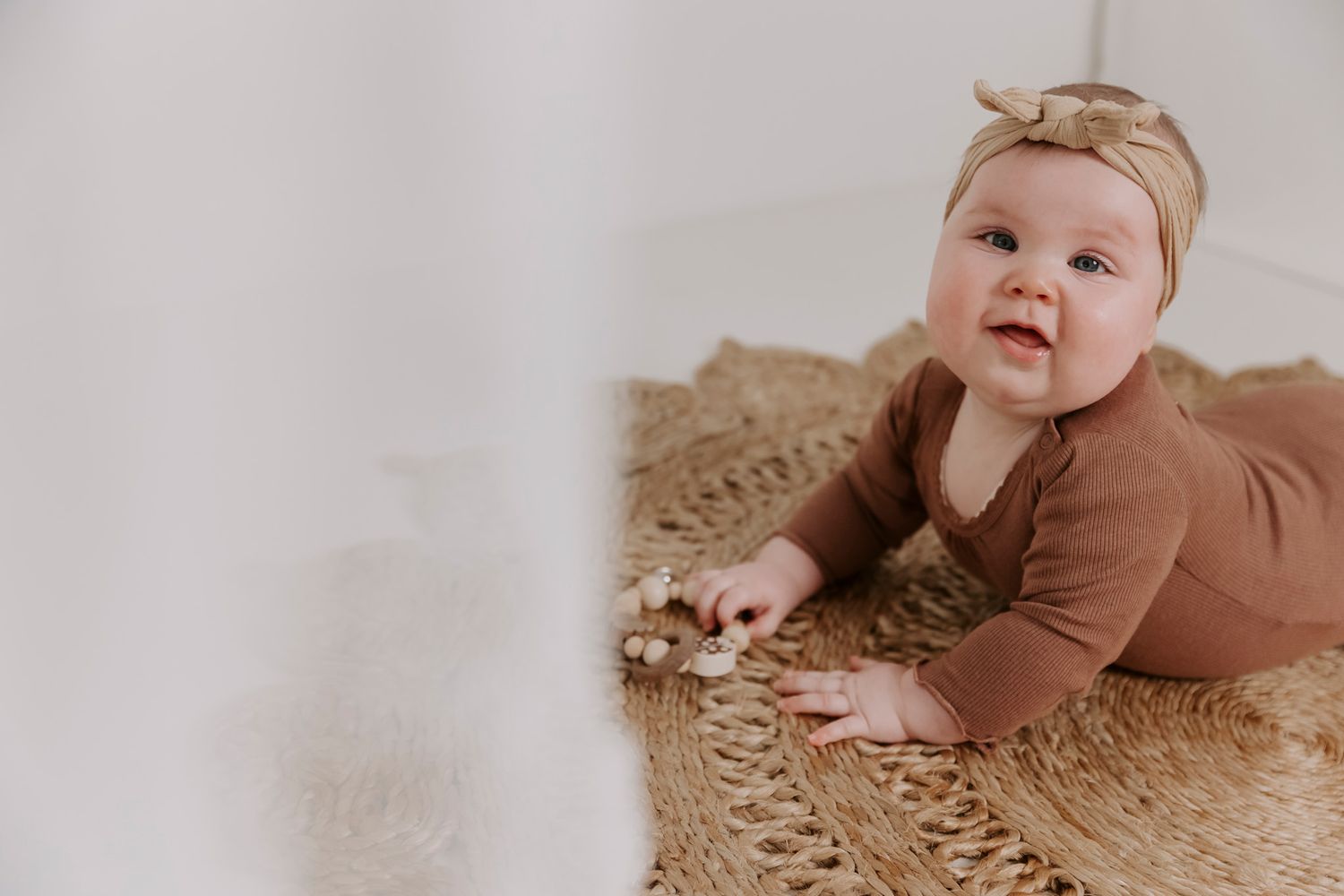 En baby i brunt outfit ligger på et tekstureret beige tæppe under en fotosession. Børnefotograf Fyn