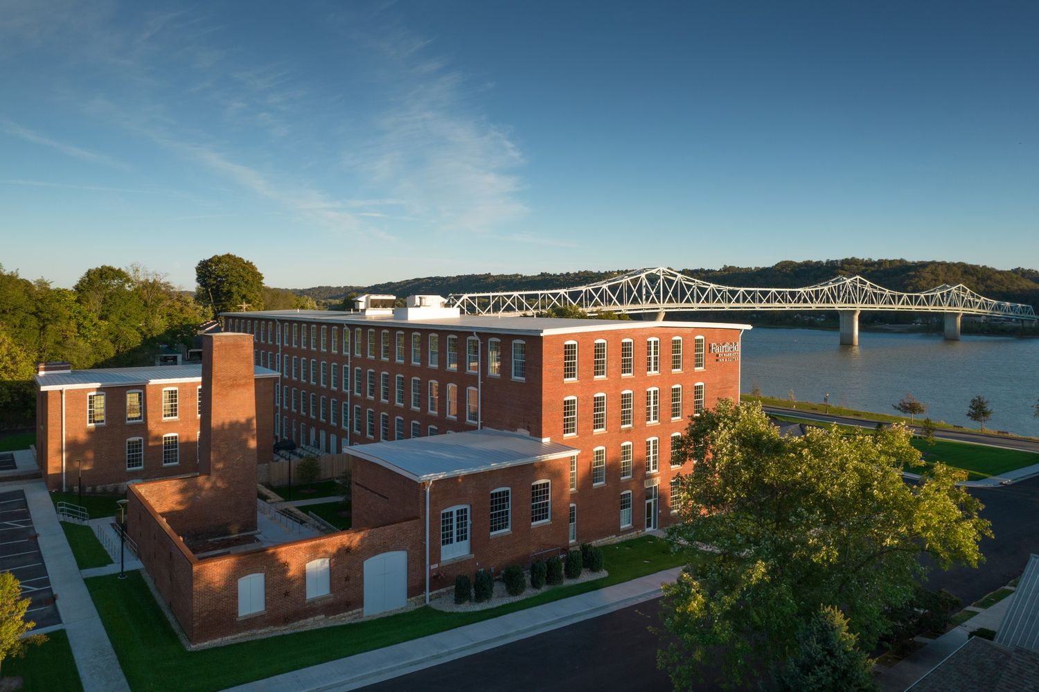 Brick office building overlooking the Hudson River with bridge and trees in scenic sunset view.