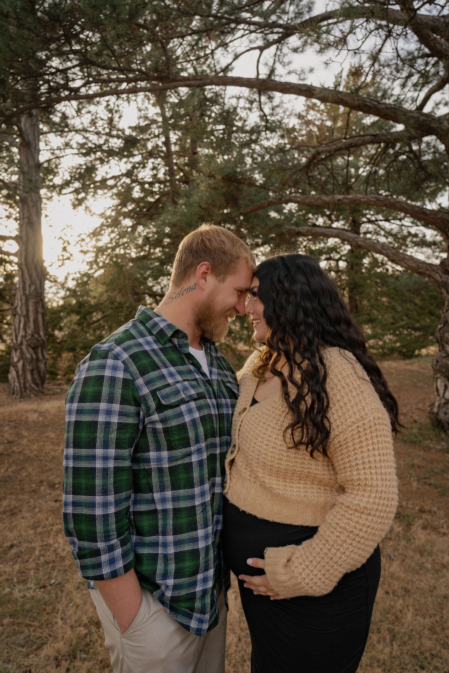 A couple in casual fall attire share an intimate moment outdoors with trees in background during golden hour.