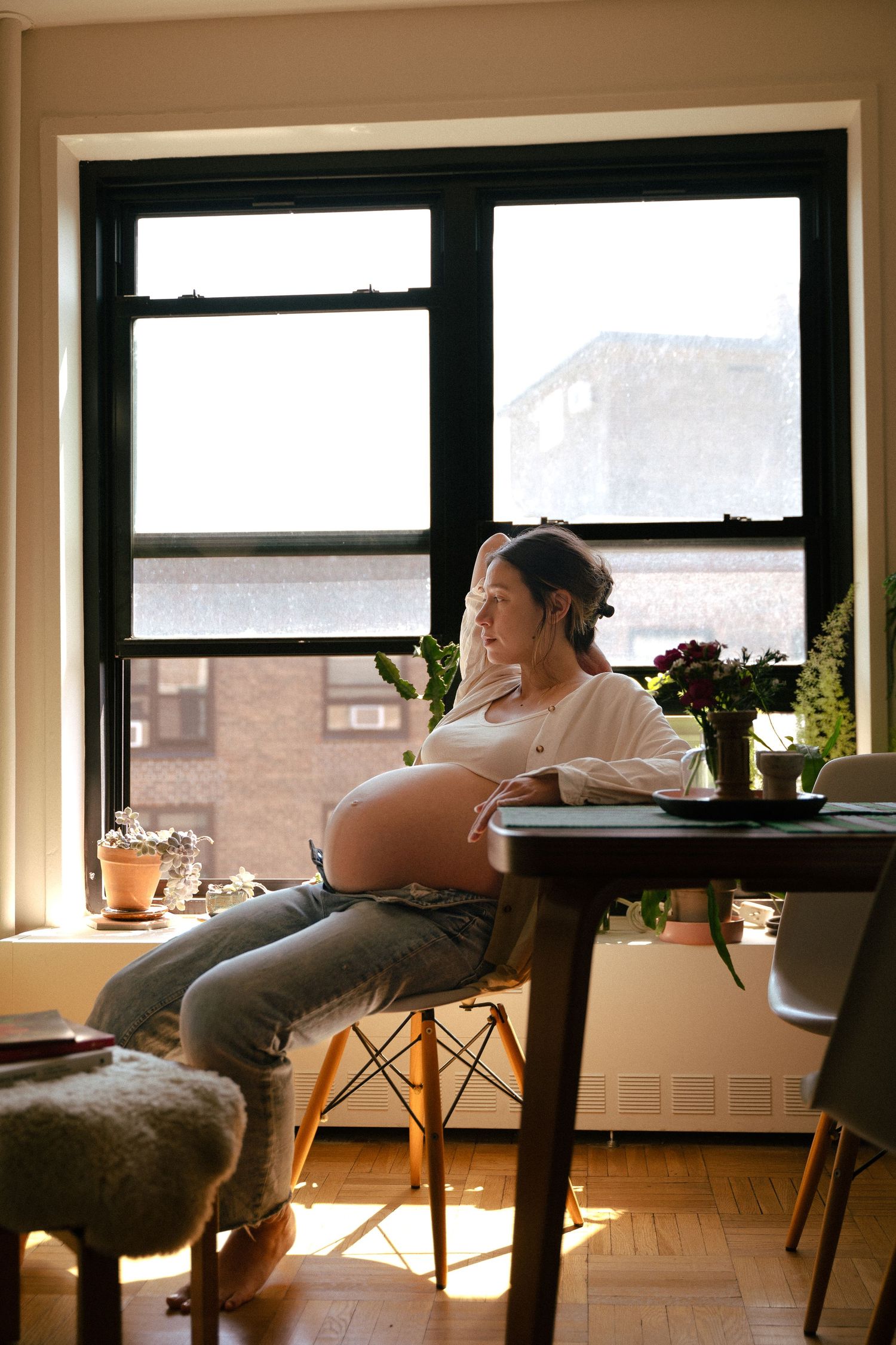 Person relaxing by window in apartment with houseplants and modern furniture during golden hour lighting.