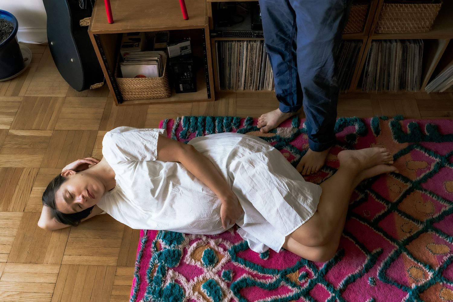 Person in white outfit lying on colorful patterned rug with record collection visible in background.