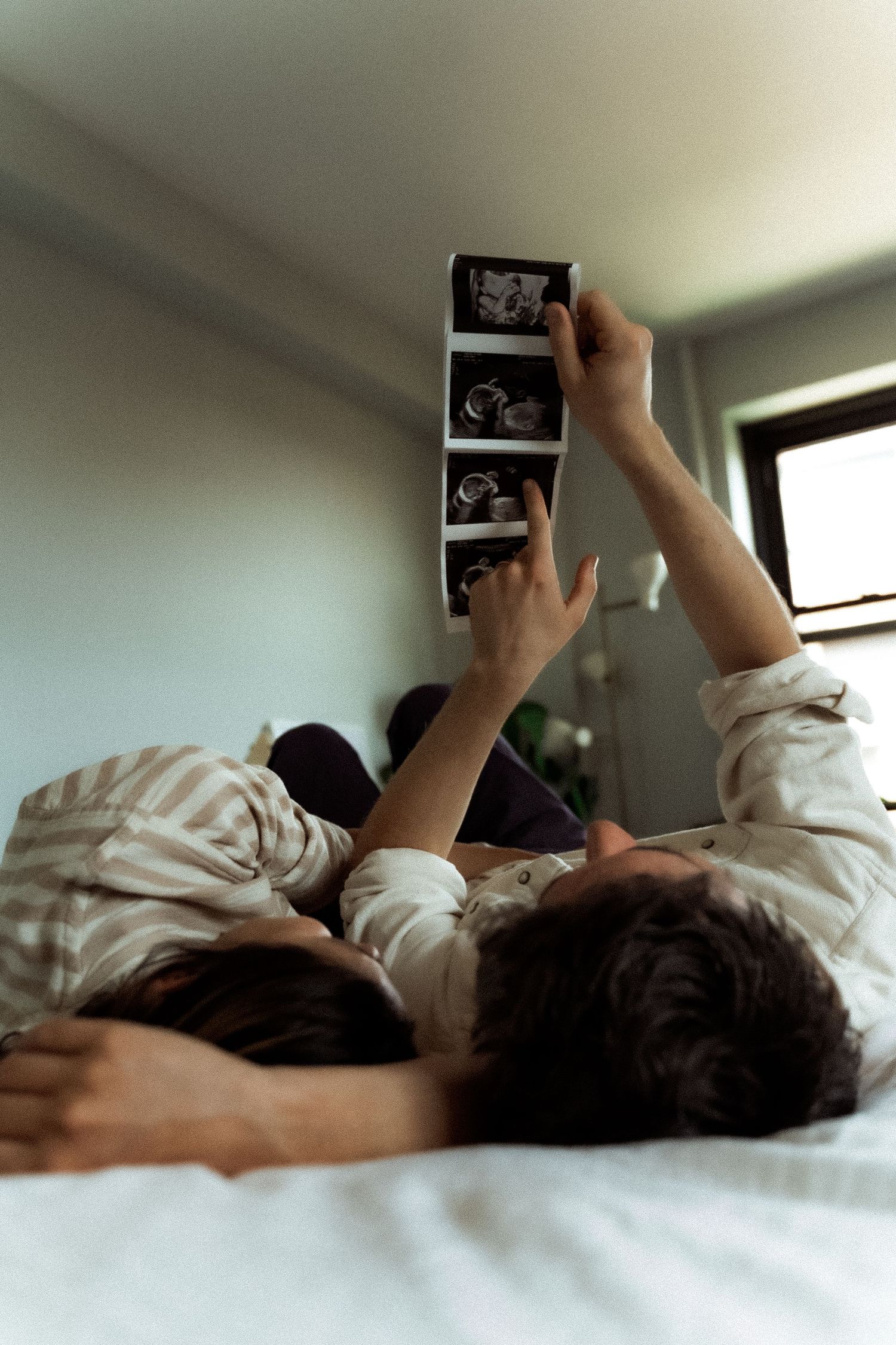 Someone lying in bed holding up what appears to be an ultrasound photo in a sequence of similar shots.
