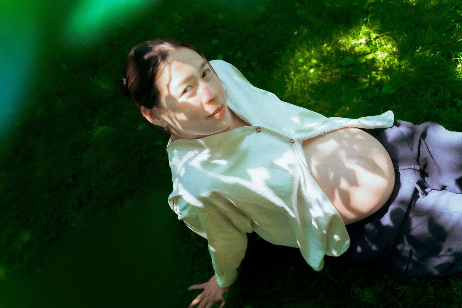 A performer in a white open shirt poses dramatically against a green nature background with dappled lighting.