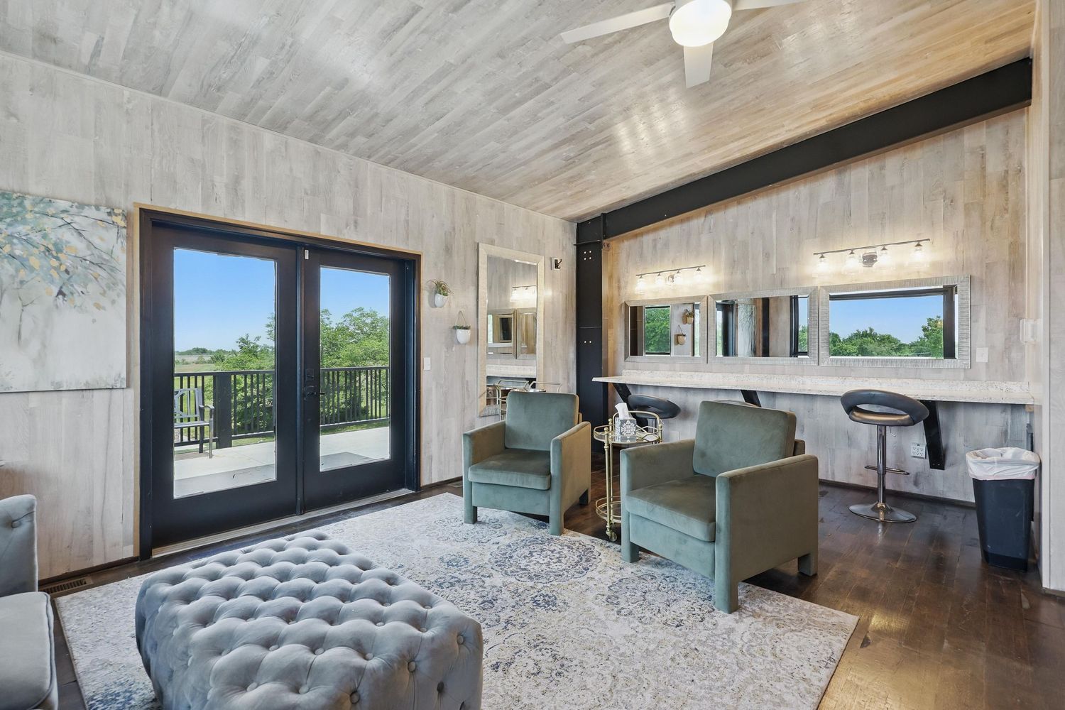 Modern home office features gray wood walls, French doors, tufted ottoman, and blue accent chairs with bar seating area.