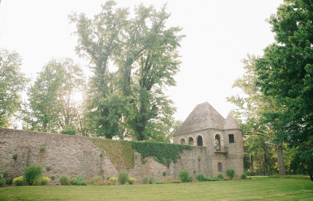 Ancient stone castle ruins with arched windows surrounded by lush green trees and manicured lawn.