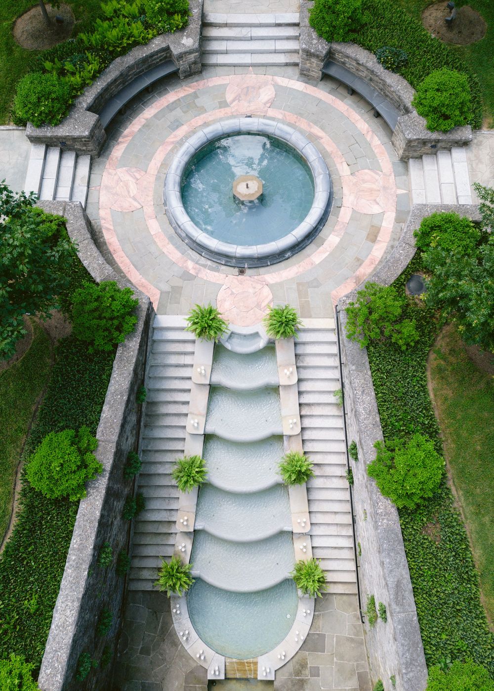 Aerial view of an elegant circular fountain garden with cascading water features and lush greenery.