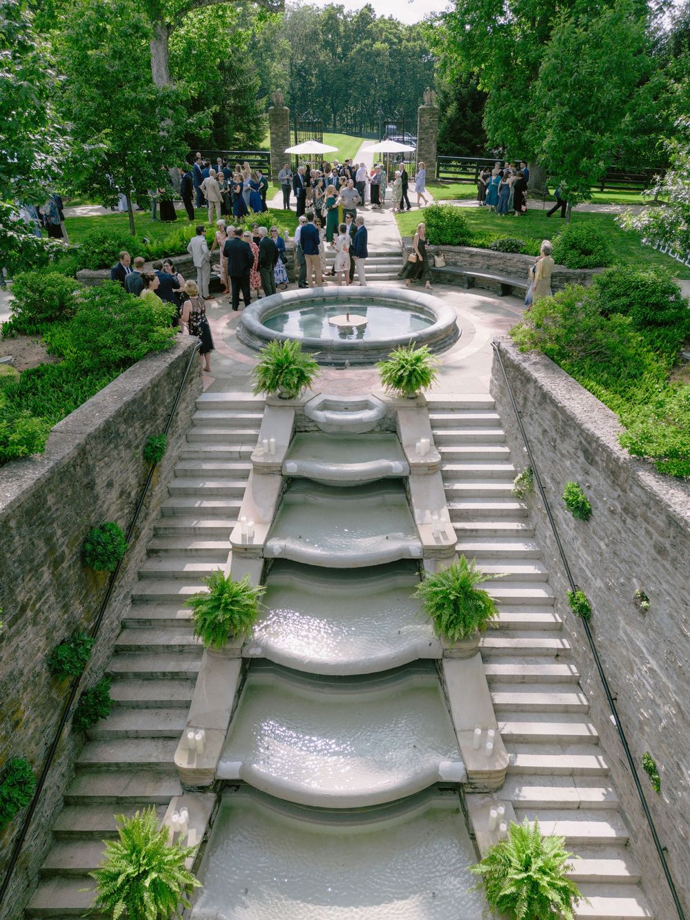 Grand cascading stone water feature staircase surrounded by lush greenery at an elegant outdoor wedding venue.