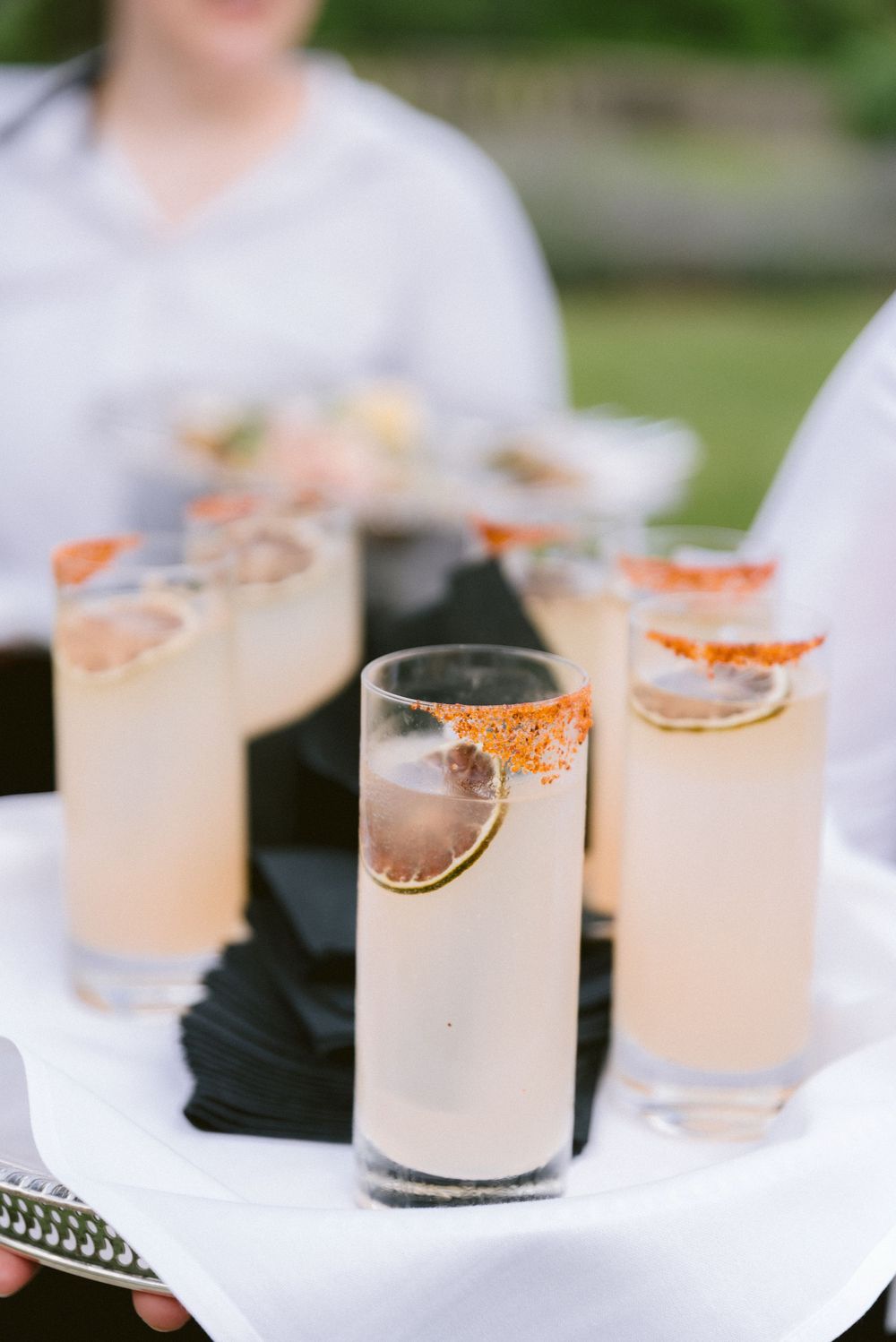 Spicy margarita cocktails with chili-rimmed glasses and lime garnish served on a tray at an outdoor event.