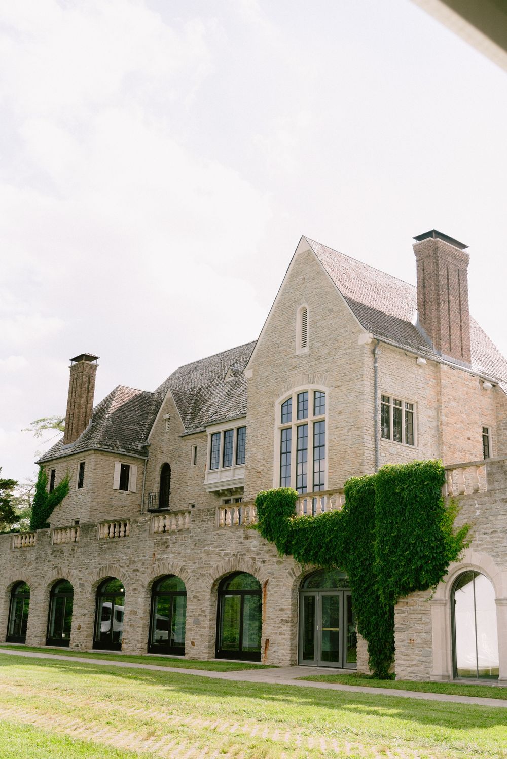 Elegant stone mansion with ivy-covered walls and arched windows set against an overcast sky.
