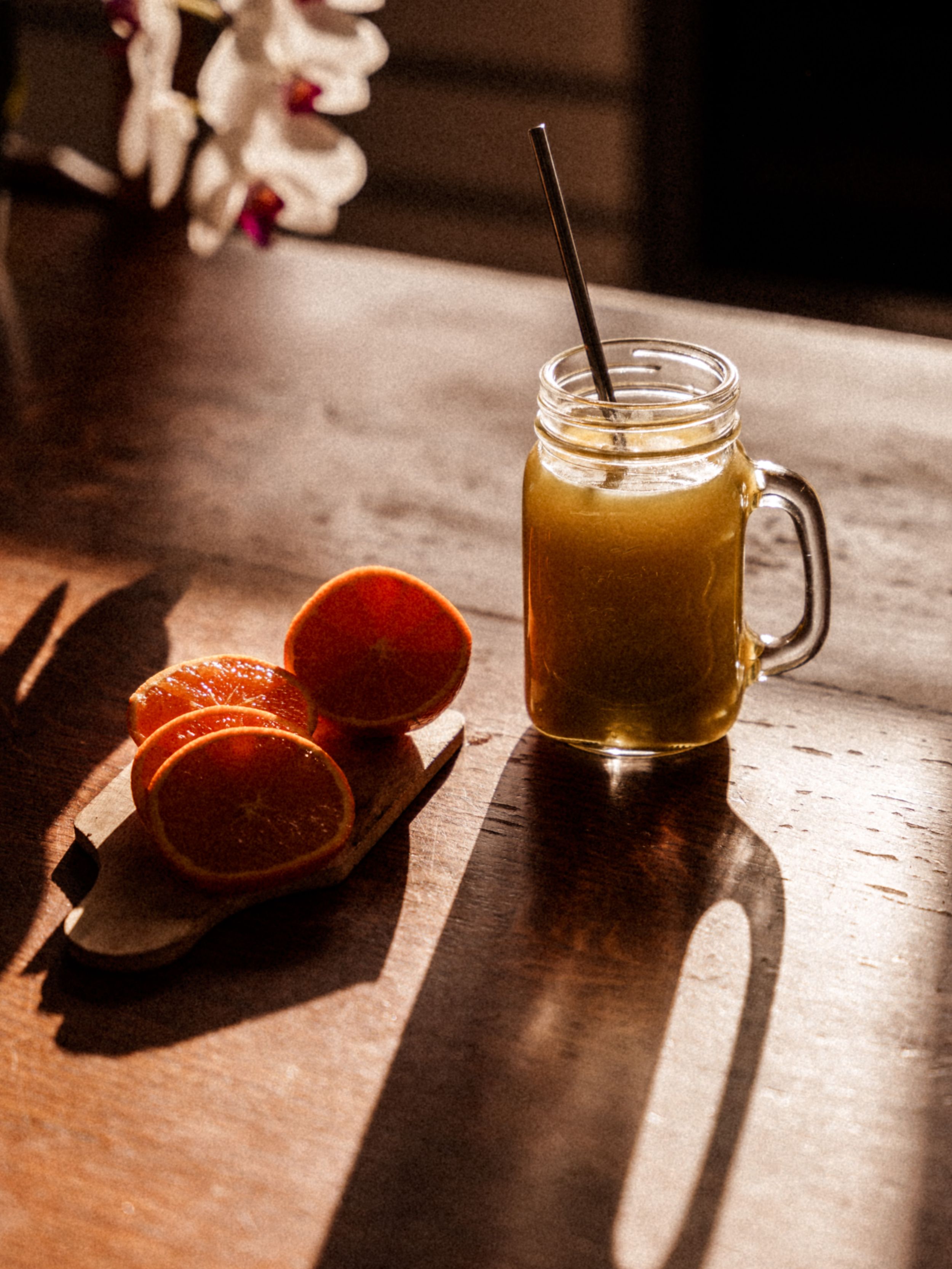 Mason jar of orange juice with fresh citrus fruits on a wooden table in dramatic lighting.