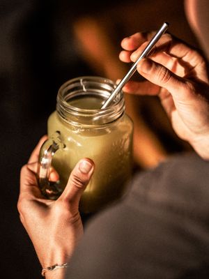 Hands holding a mason jar filled with a creamy brown smoothie and metal straw in moody lighting.