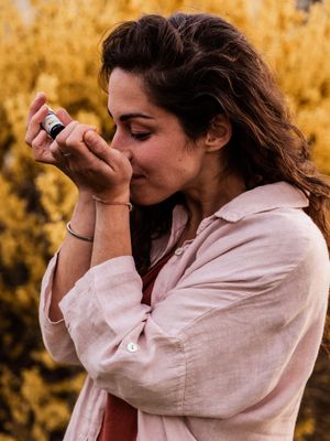 A person playing a harmonica against a backdrop of golden autumn foliage while wearing a light pink button-down shirt.