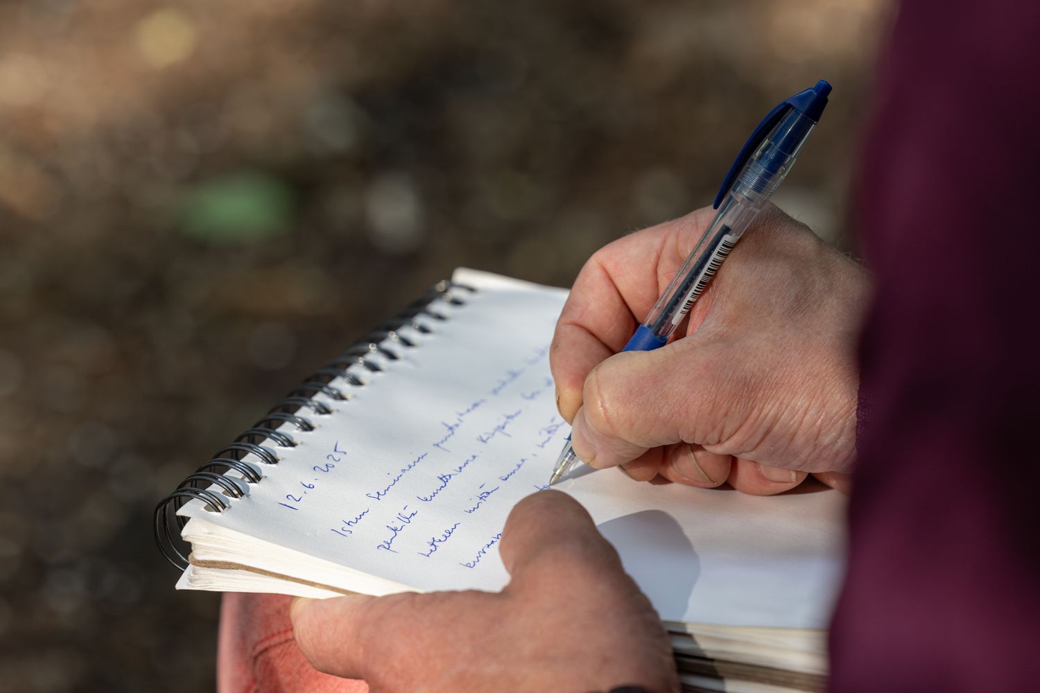 A hand writes notes in a spiral notebook with a blue pen against a dark background.