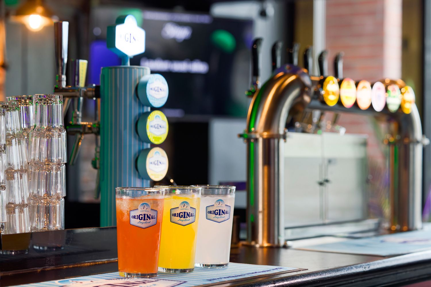 Three colorful draft beers on a bar counter next to tap handles in a modern pub setting.