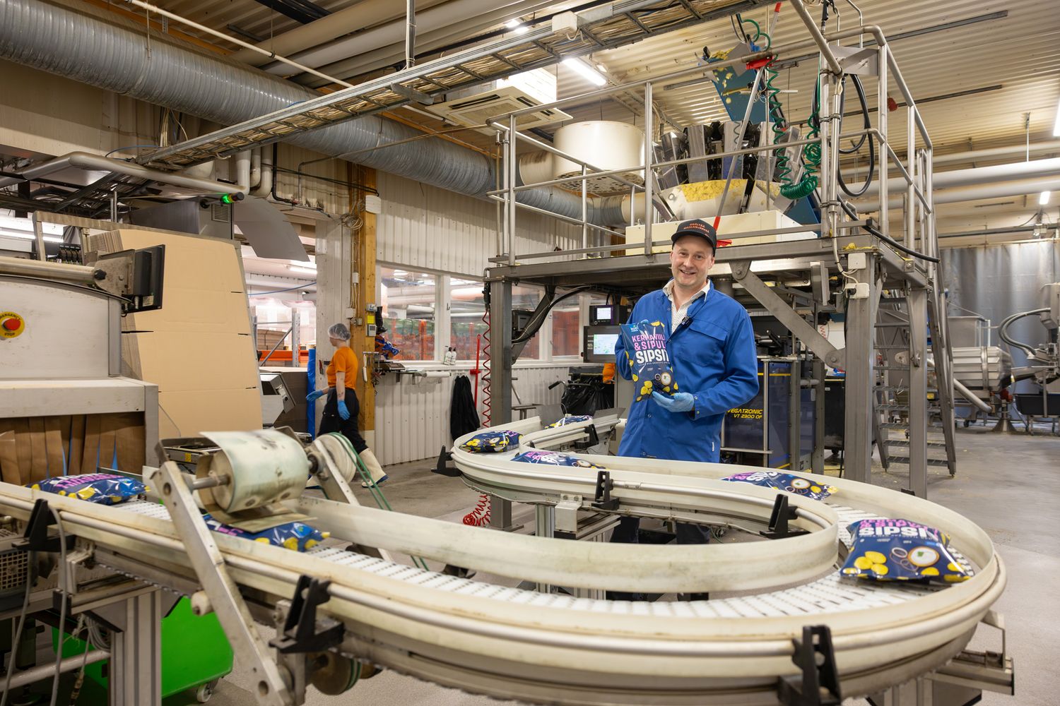 Worker in blue uniform stands beside curved conveyor belt system in modern food packaging factory.